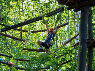 A person in a helmet and harness lying on a suspended net bridge, navigating the obstacle in a ropes course.