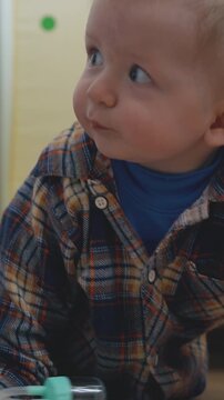 funny little baby in checkered shirt scrawls and leans on soft bed on wooden floor in children room close view