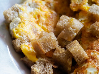 A detailed, eye-level shot of a homemade breakfast of scrambled eggs with brown bread pieces and melted cheese, served in a white bowl.
