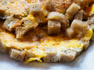 A vibrant close-up of a rustic and appetizing dish of scrambled eggs with golden-brown fried bread pieces and a hint of melted cheese.