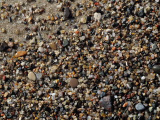A close-up view of a sandy beach surface with a few small pebbles, creating a clean, minimalist, and natural background.