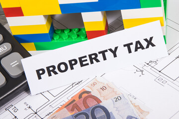 Inscription property tax, euro banknotes, calculator, house made of toy blocks and electrical installation plan. Increasing real estate taxation