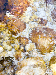 bright riverbed with colorful stones under rippling crystal clear water. vivid reflections. abstract natural texture. clean design. wellness, eco concept