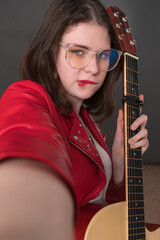 Female influencer guitarist biting her lip in playful expression takes selfie of herself with guitar in her hand, creating user-generated content