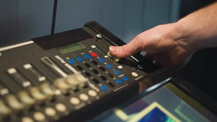 A person adjusts a professional sound or video equipment control panel. Focused on setting or adjusting controls on a complex device with buttons, dials, and screen. Shot in low light setting