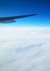 Plane wing on vivid blue sky with sea of clouds view from plane window during flight