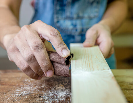 A craftsman's hands sand a wooden board.