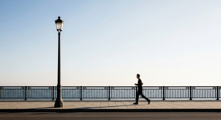Silhouette of man jogging near ocean railings at dusk