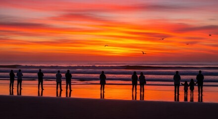 Silhouetted figures stand on a beach, watching a vibrant orange and red sunset over the ocean.