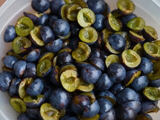 Fresh, halved blackthorns in a bowl, prepared for cooking or preserving.