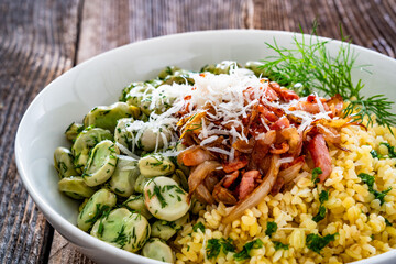 Boiled broad beans with bulgur, fried bacon and onion on wooden table	