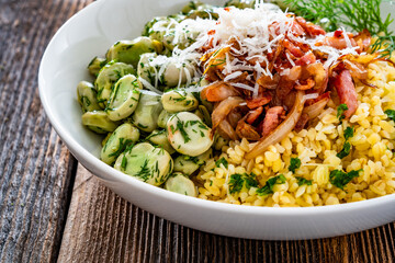 Boiled broad beans with bulgur, fried bacon and onion on wooden table	