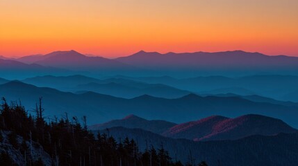 A mesmerizing mountain range layered in shades of blue fades into the horizon, capped by a fiery sunset of orange and pink hues