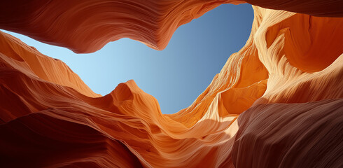 A wide-angle photo of the interior of Antelope Canyon, with a blue sky and warm sunlight shining through the sandstone rock formations