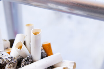 A detailed, close-up shot shows a cluster of burnt-out cigarettes and butts with their filters exposed, filling a rusty or old ashtray