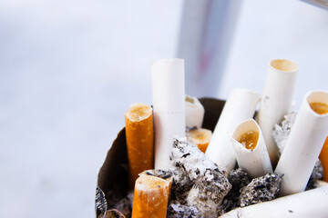 A detailed, close-up shot shows a cluster of burnt-out cigarettes and butts with their filters exposed, filling a rusty or old ashtray