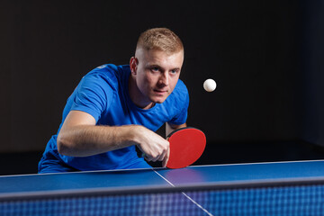 Focused table tennis player returning ball with red paddle during indoor match