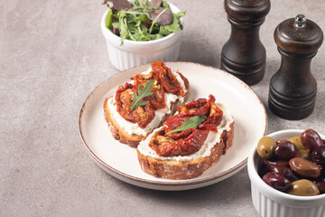 Two bruschettas with dried tomatoes, ricotta cheese and rucola on ciabatta bread. 