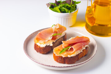 Two bruschettas with prosciutto, ricotta cheese and rucola on ciabatta bread. Olive and spices  decorated.