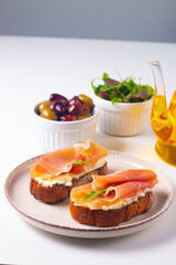 Two bruschettas with prosciutto, ricotta cheese and rucola on ciabatta bread. Olive and spices  decorated.