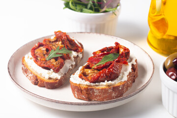 Two bruschettas with dried tomatoes, ricotta cheese and rucola on ciabatta bread. 