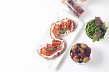 Two bruschettas with dried tomatoes, ricotta cheese and rucola on ciabatta bread. 
