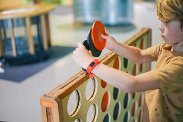 Young boy playing giant connect four game with red and black disks