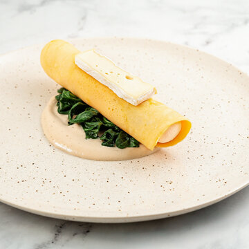French omelette with spinach and Brie cheese on a ceramic plate. Gourmet French omelette stuffed with spinach and creamy Brie cheese, served on a ceramic plate with elegant restaurant-style presentati