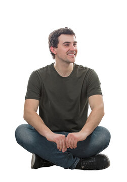 Cheerful young man seated relaxed, with crossed legs, on the floor, looking away smiling isolated on transparent background