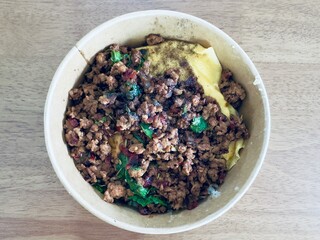 This image shows a close-up, top-down view of a take-out bowl filled with a popular Thai dish, likely Pad Krapow.