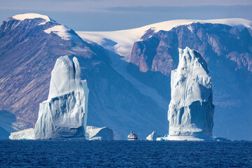 A pair of blue towering icebergs appear to form gates in Ofjord, or O fjord, Scoresby Sund, Greenland. A ship appears between them to give an idea of scale, with snow covered mountains behind. © Rixie