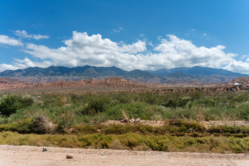Mountain landscape view from dirt road south of Issyk Kul, Kyrgyzstan showing Tian Shan mountain range with weathered formations and green vegetation.