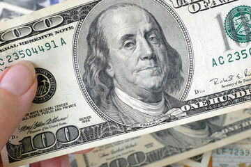 hand with magnifying glass checking 100 USA dollar banknote on money background, exchange money