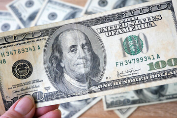 hand with magnifying glass checking 100 USA dollar banknote on money background, exchange money