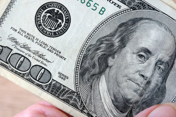 hand with magnifying glass checking 100 USA dollar banknote on money background, exchange money