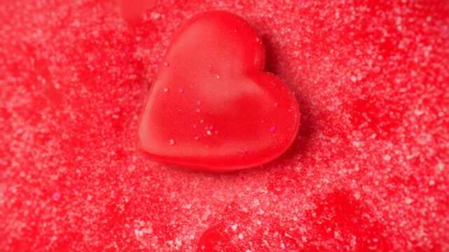 Close-up of red heart-shaped candies and sprinkles rotating, creating a vibrant, textured pattern in bright lighting