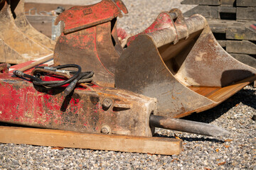 Hydraulic chisel on the ground of a construction site. Behind some excavator buckets.