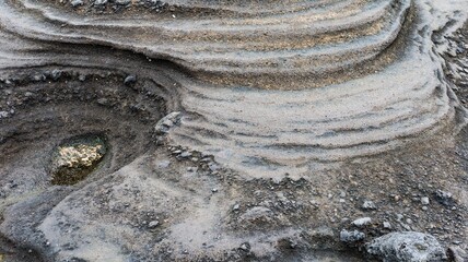 Close up of undulating layers in dark volcanic rock stone layers with subtle golden streaks, sand...