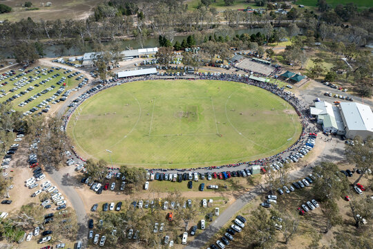 Aerial view of players and crowd at a rural Australian rules football match.