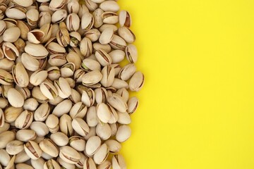 Tasty unpeeled pistachios on bright yellow background, top view flat lay background pattern