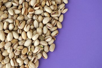Tasty unpeeled pistachios on bright purple background, top view flat lay background pattern