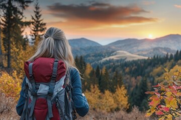 Fototapeta premium A woman gazes at a stunning sunset over mountains, surrounded by autumn colors, embodying the spirit of adventure and nature.