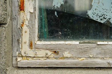 Close-up view of a vintage wooden window frame displaying extensive wear, peeling paint, and damaged glass, captured in a rural area.