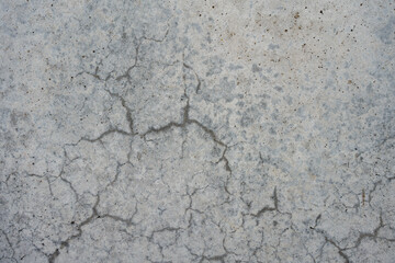 Close-up of cracked gray concrete surface with visible texture. The natural pattern of cracks creates an abstract background.