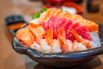 Fresh assorted sashimi platter with salmon, tuna, and shrimp served on crushed ice in a black bowl, showcasing vibrant colors and premium seafood for Japanese cuisine lovers.