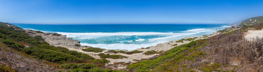 Panoramic view of a rugged coastline with turquoise ocean waves crashing onto sandy shores