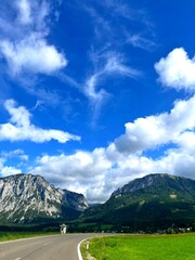 Curved road through scenic alpine valley with rocky mountains and blue cloudy sky in Austria. Beautiful travel and adventure landscape perfect for tourism and exploration.