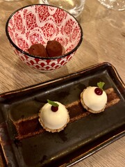 Elegant dessert platter with white chocolate spheres and chocolate truffles in decorative ceramic bowls on wooden table