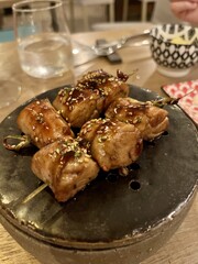 Grilled meat skewers with glaze and sesame seeds on dark ceramic plate in Italian restaurant