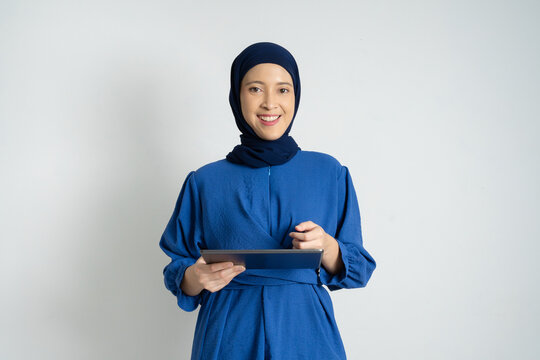 A young woman wearing a blue hijab and dress cheerfully holding a tablet. The image conveys professionalism, confidence, and modern technology in a multicultural context.